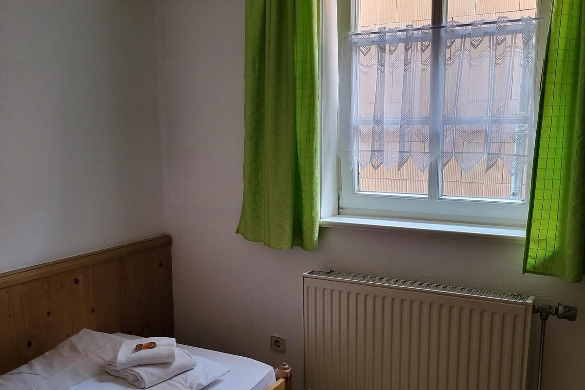 A small, single-bed room with a wooden headboard, a radiator, and a window with green curtains.