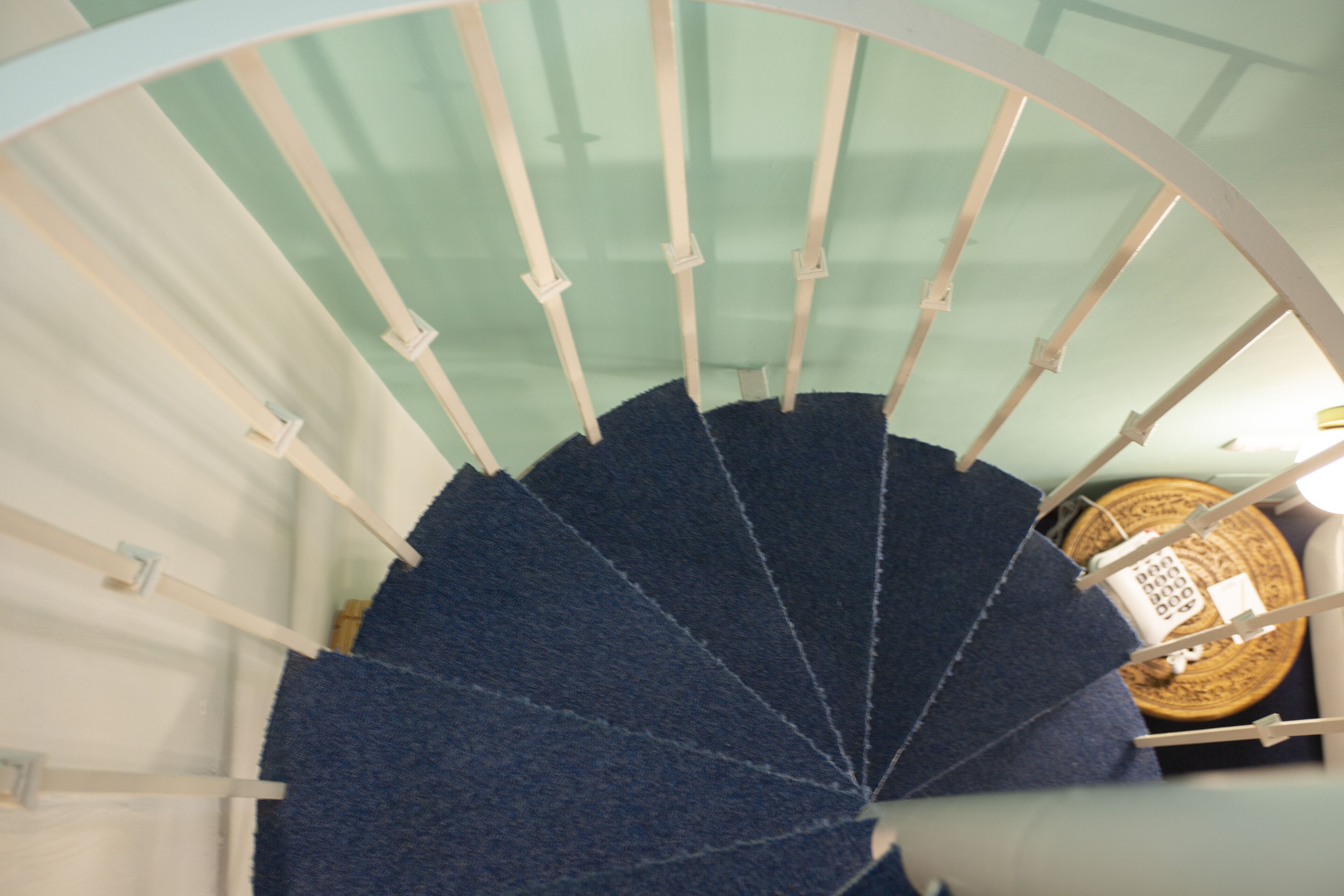 A spiral staircase with a blue carpet and white balusters.