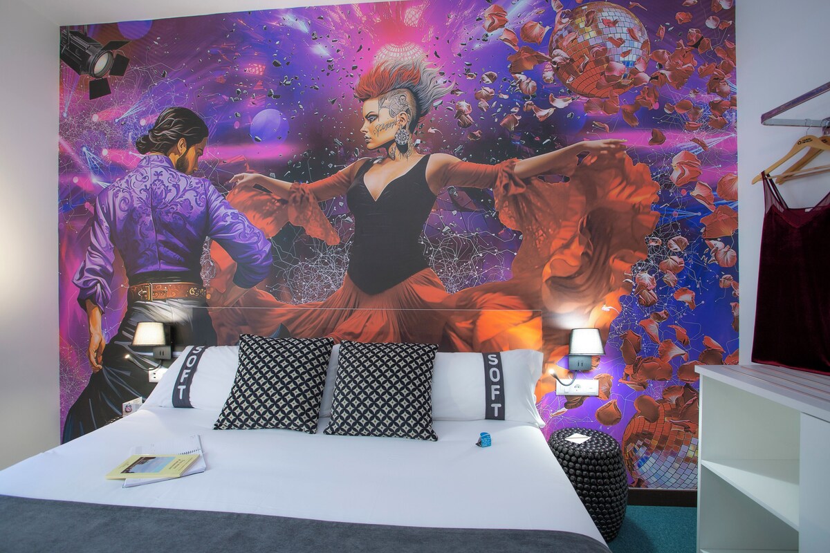 Quarto com um mural grande, uma cama com almofadas estampadas e uma mesa de cabeceira com abajur.