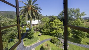 A view of a lush garden with a palm tree, a swimming pool, and a pathway leading to a white building. - Pazo da Trave (Viveiro)