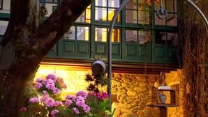 A stone building with green shutters, a tree with pink flowers, and a metal archway. - Pazo da Trave (Viveiro)