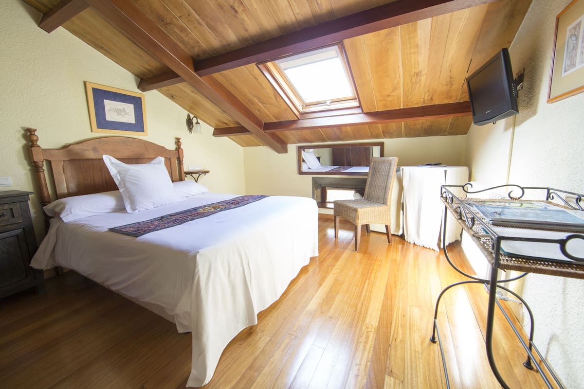 A bedroom with a wooden ceiling, a bed with white bedding, a chair, a desk, and a television.