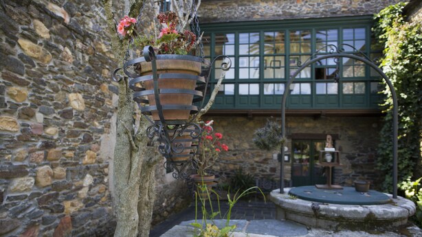 A stone building with a hanging flower pot and a small fountain. - Pazo da Trave (Viveiro)