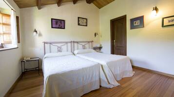 A bedroom with two beds, wooden flooring, a small bedside table, and a door.
