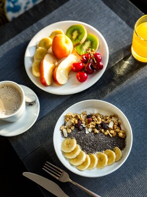 A breakfast setting with two plates of fruit and granola, a cup of coffee, and a glass of orange juice on a table. - Room Mate Leo, Granada (Granada)