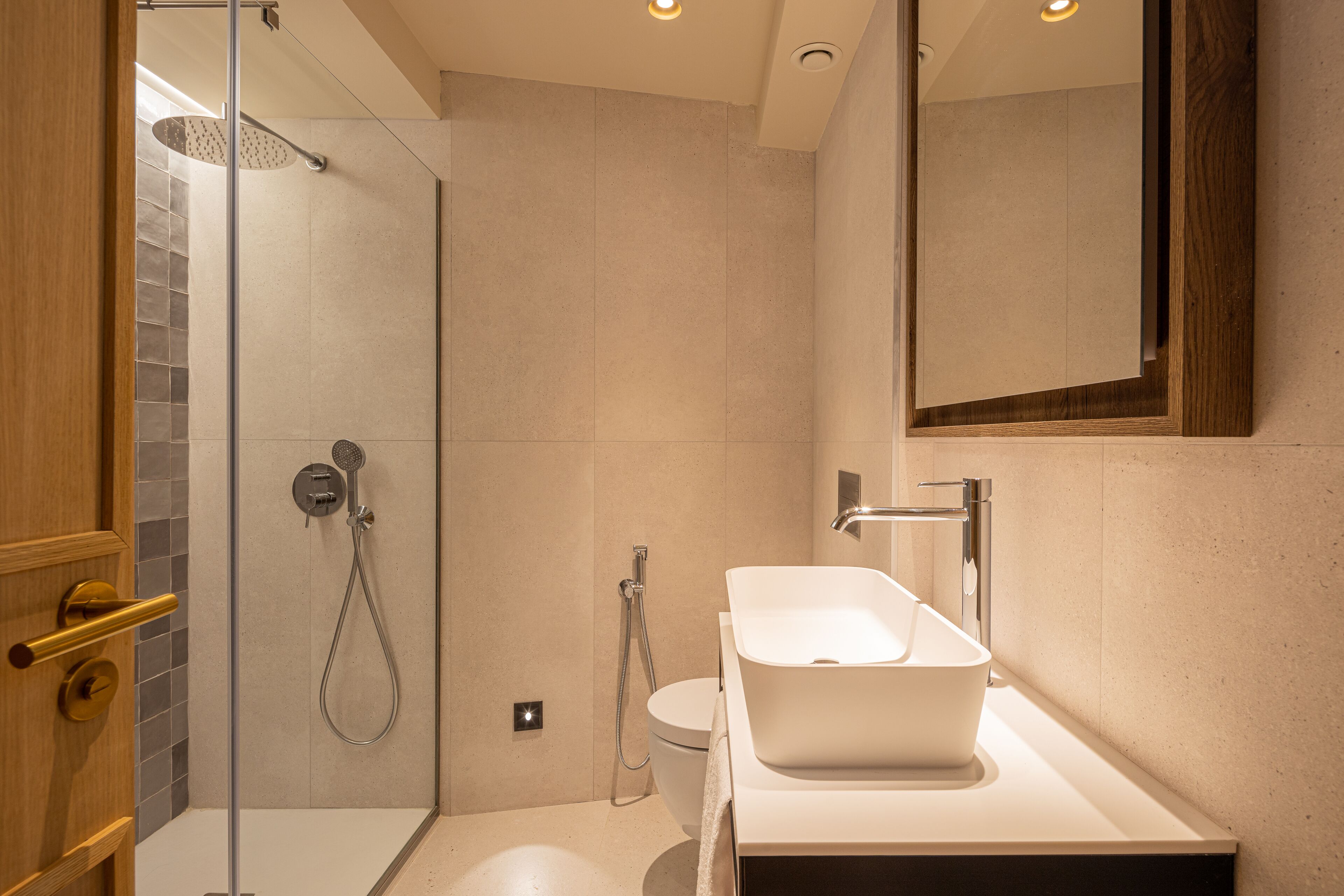 Un baño moderno con ducha de vidrio, un lavamanos blanco y un espejo grande.