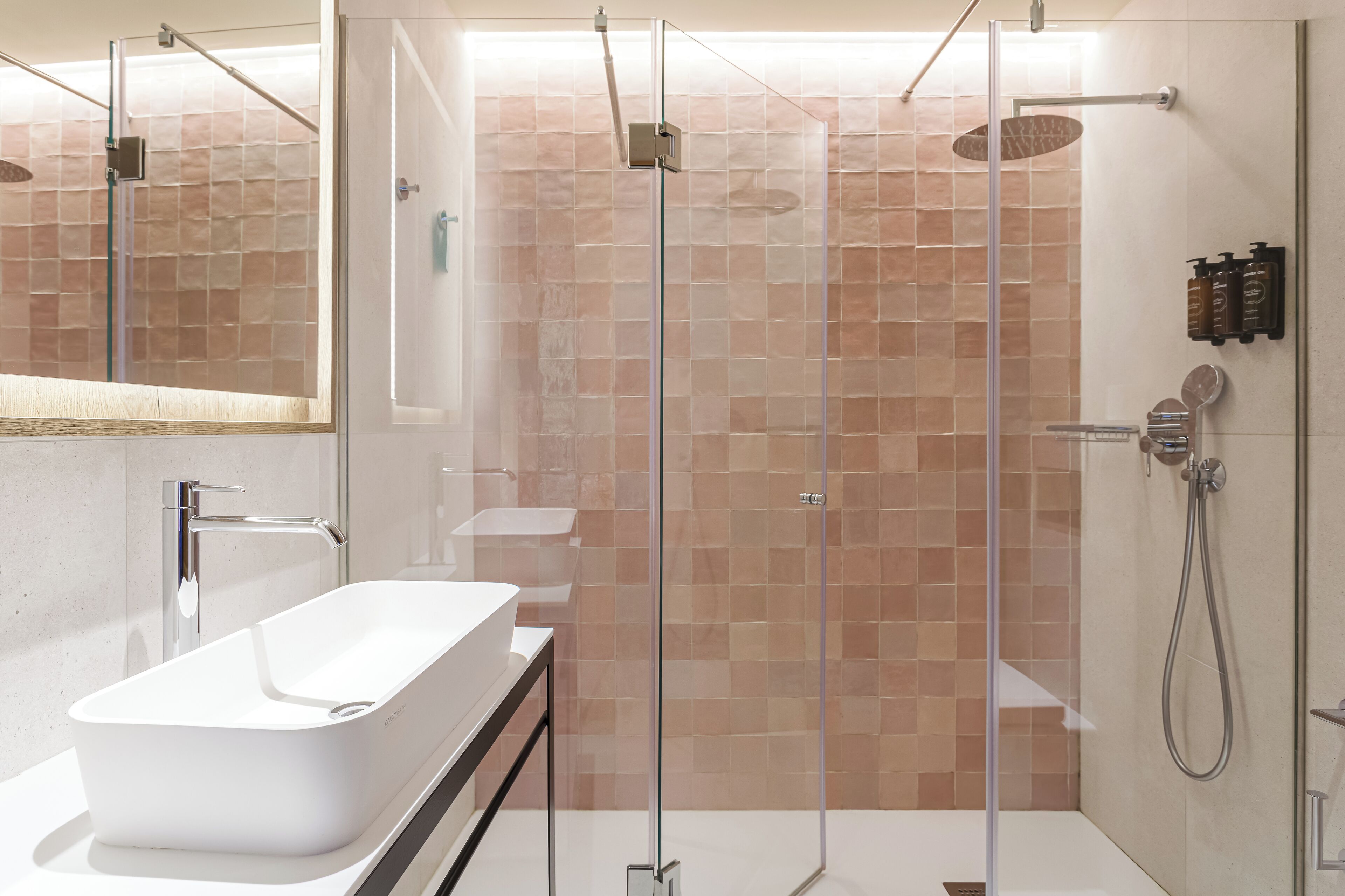A modern bathroom with a glass-enclosed shower, a white sink, and a tiled shower wall.