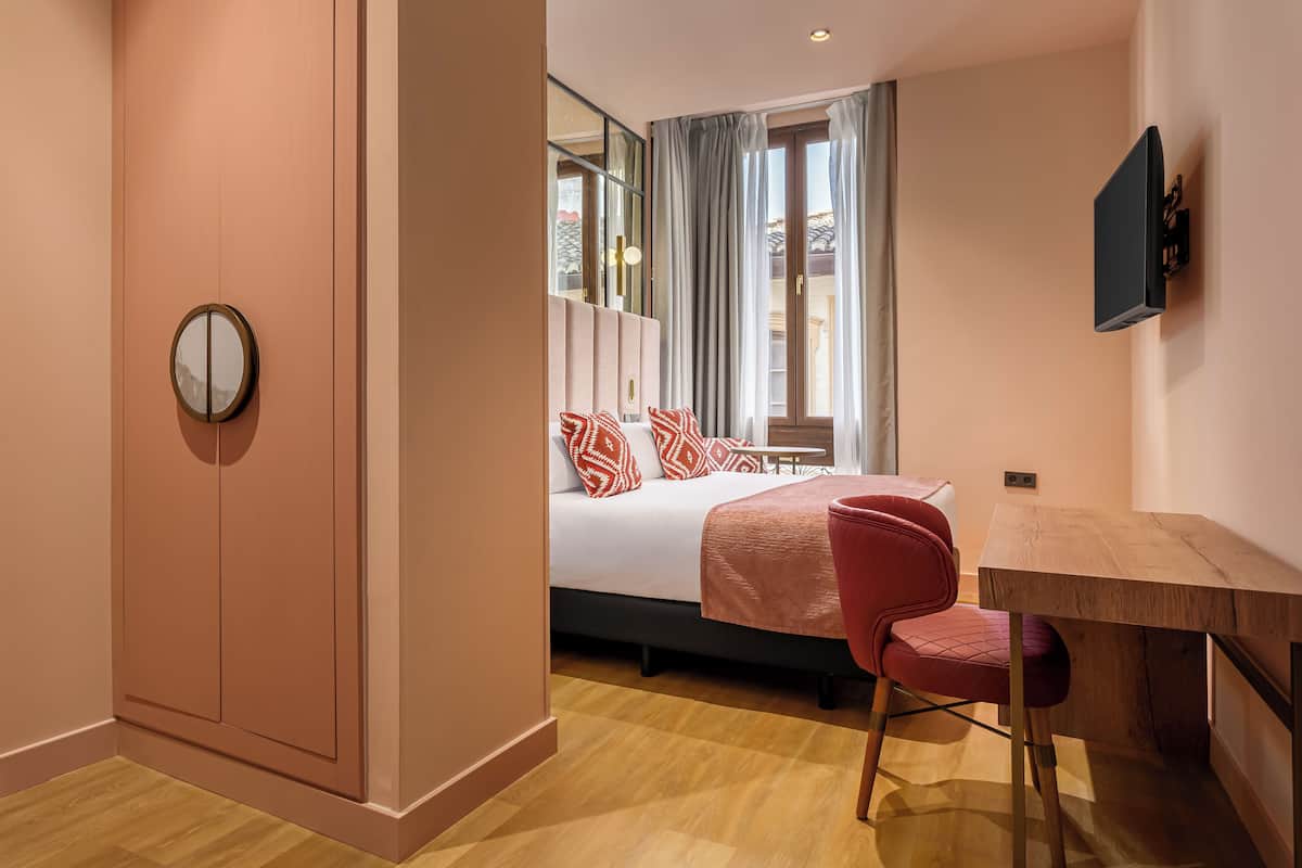 Ein Hotelzimmer mit Bett, Schreibtisch, Stuhl, Fernseher und einem Fenster mit Vorhängen.