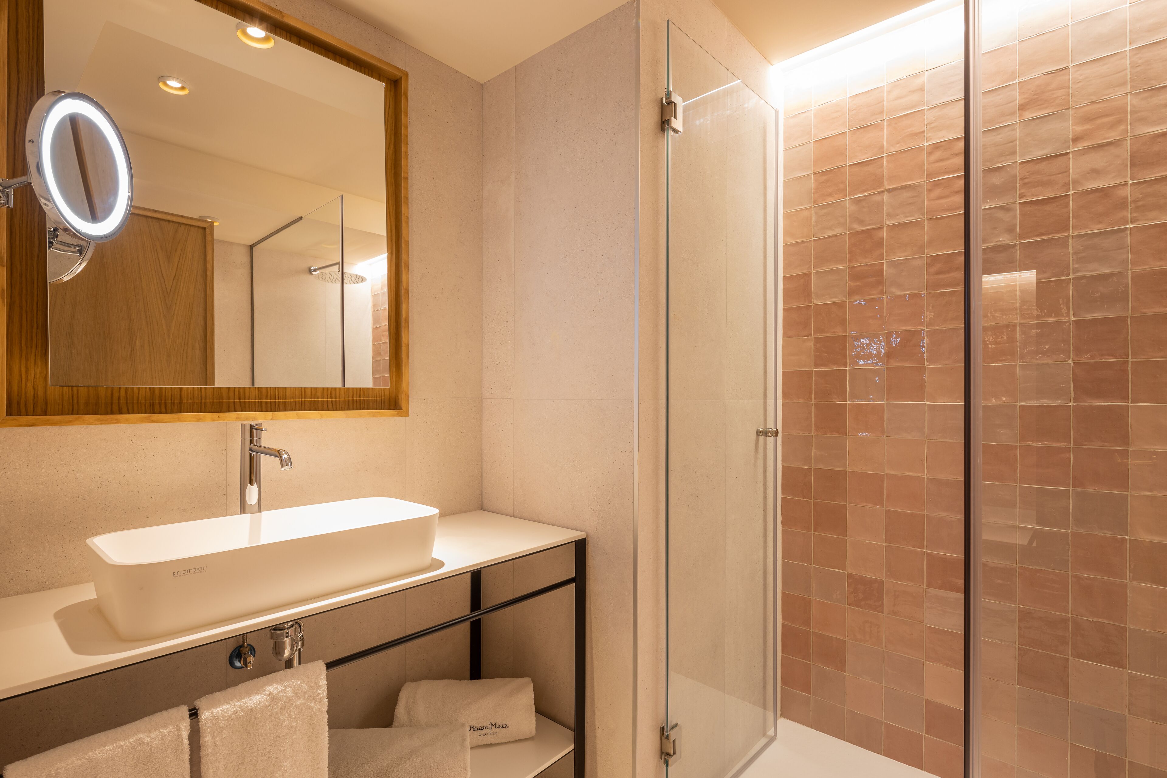 Un baño moderno con cabina de ducha de vidrio, un lavabo blanco y un espejo con luz.