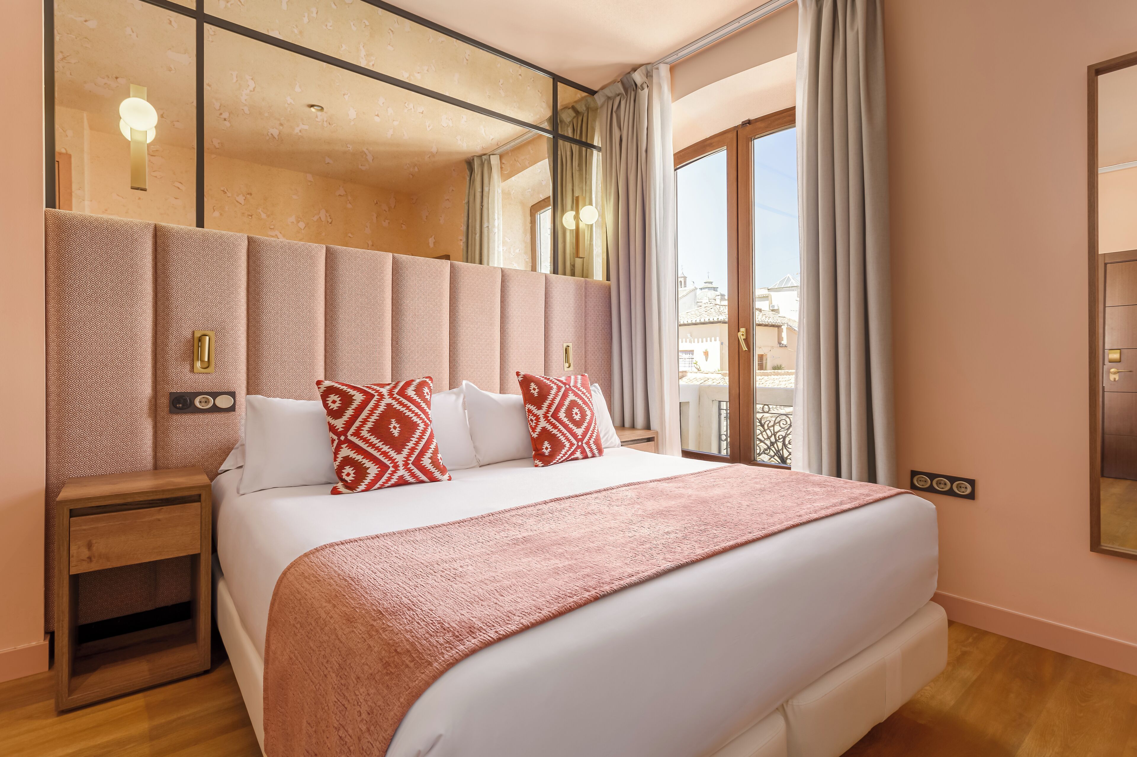 Habitación de hotel con una cama grande, una mesita de noche, un espejo y vistas al exterior.