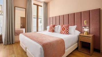 Habitación de hotel con una cama grande, una mesita de noche de madera con una lámpara, un espejo y vistas a un balcón.