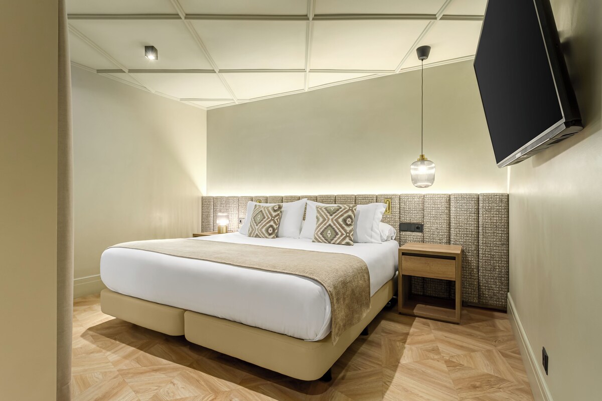 A modern bedroom with a large bed, bedside tables, a TV, and a hanging light fixture.