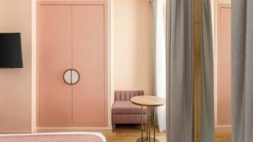 Una habitación de hotel con un armario rosa, una mesa redonda, un sofá y un televisor montado en la pared.