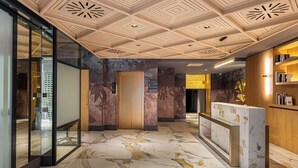 A modern hotel lobby with marble flooring, a reception desk, and a ceiling with geometric patterns.