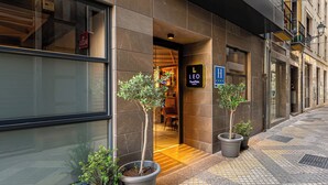 A modern building with a glass entrance, potted plants, and a sign indicating a hotel.