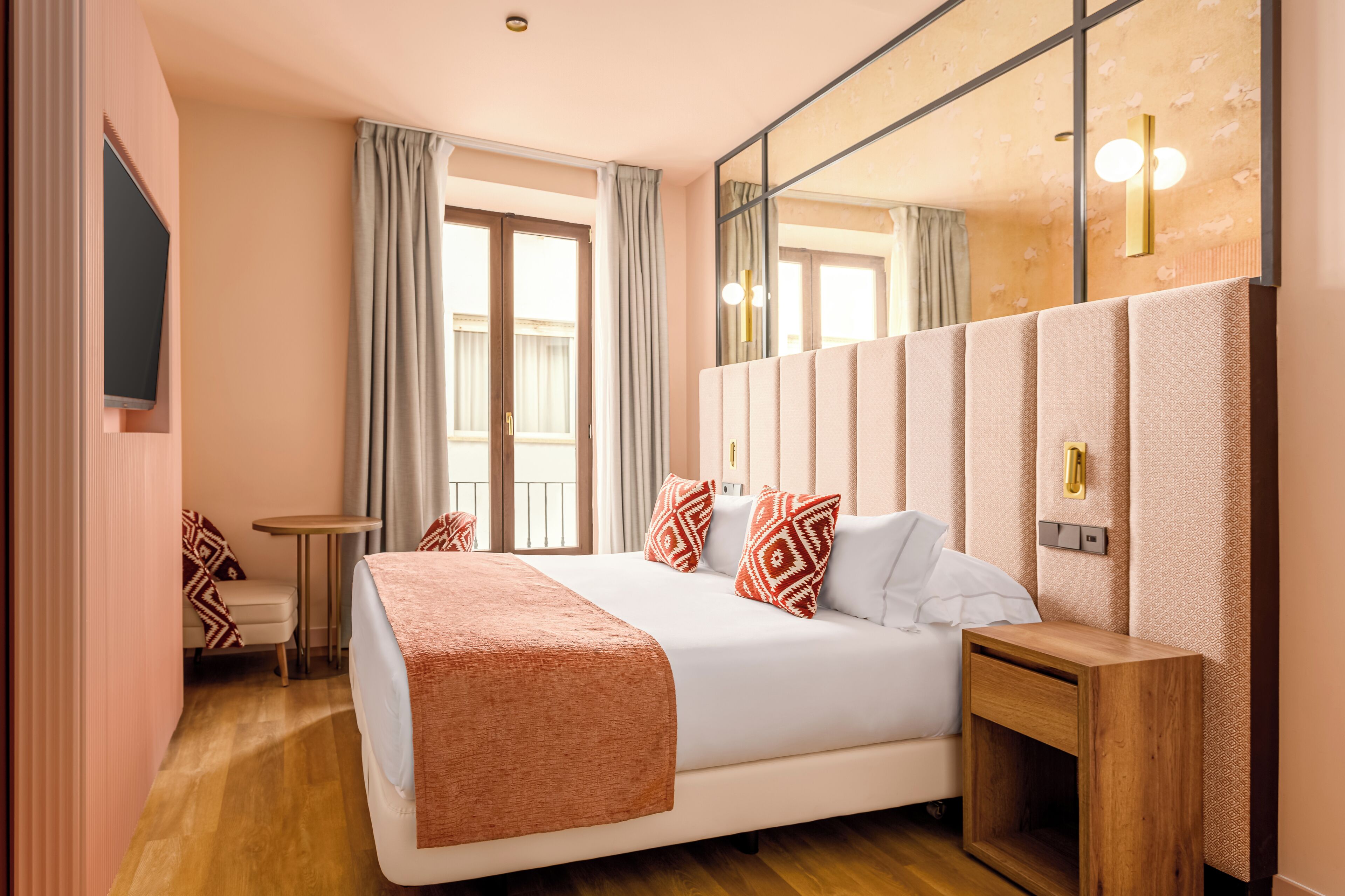 Habitación de hotel con una cama grande, una mesita de noche, una pequeña mesa, un televisor montado en la pared y un espejo amplio.