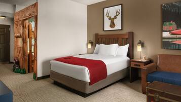 Une chambre d’hôtel avec un grand lit, une tête de lit en bois, un plaid rouge, une table de chevet avec une lampe, une valise et un tableau représentant un cerf accroché au mur.