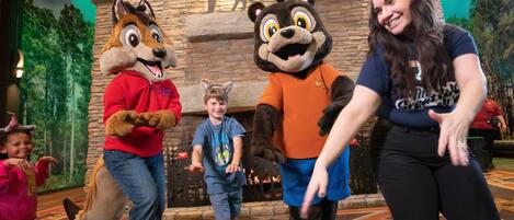 A person in a bear costume and two children in front of a stone wall with animal silhouettes.