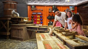 Un intérieur rustique avec des tables en bois, un tonneau et un mur où sont exposés des objets aux couleurs vives.