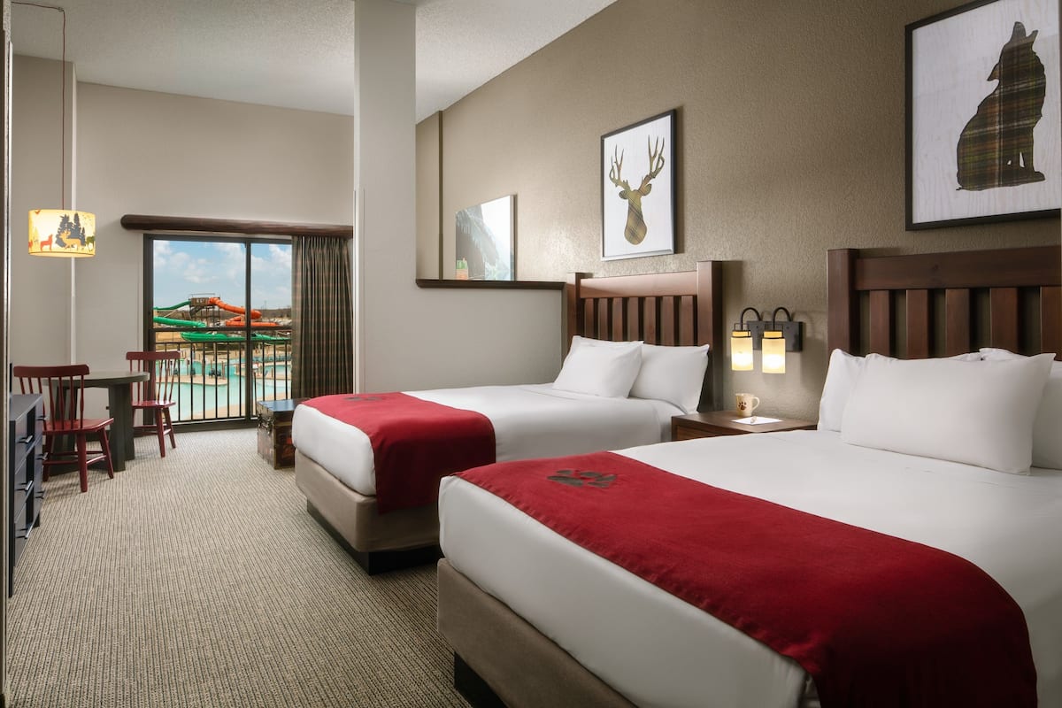 A hotel room with two beds, a desk, chairs, and a view of a water park.