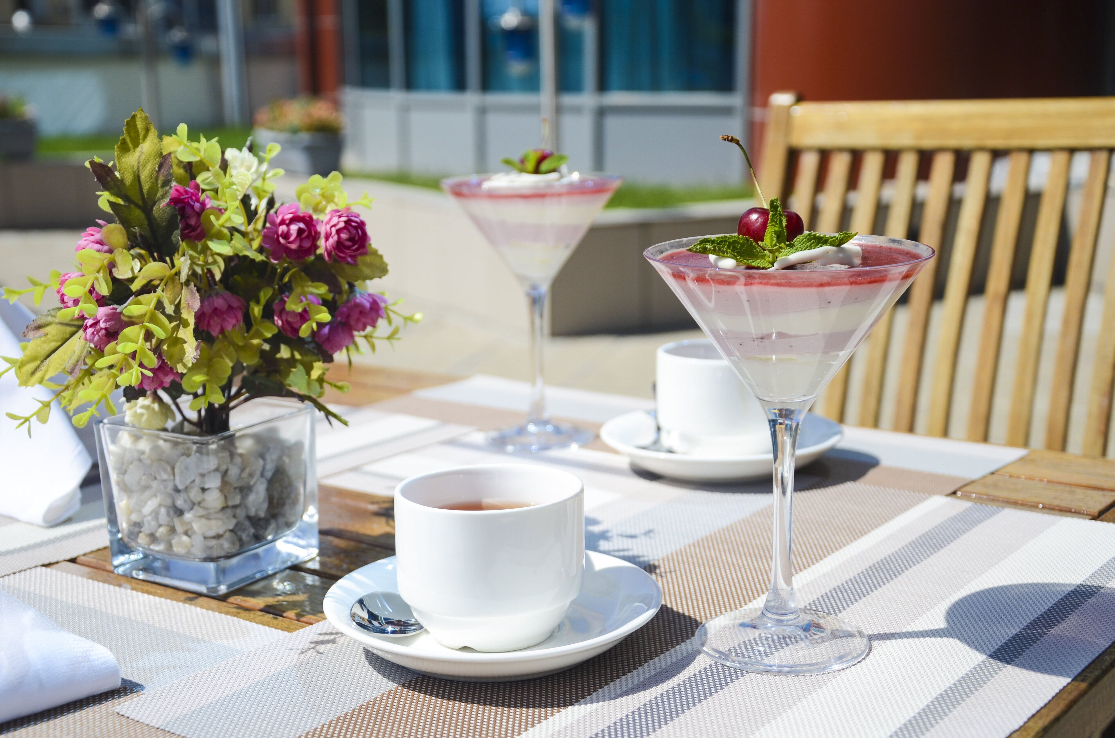 A table set with a white cup, a martini glass, and a dessert glass, accompanied by a floral arrangement.