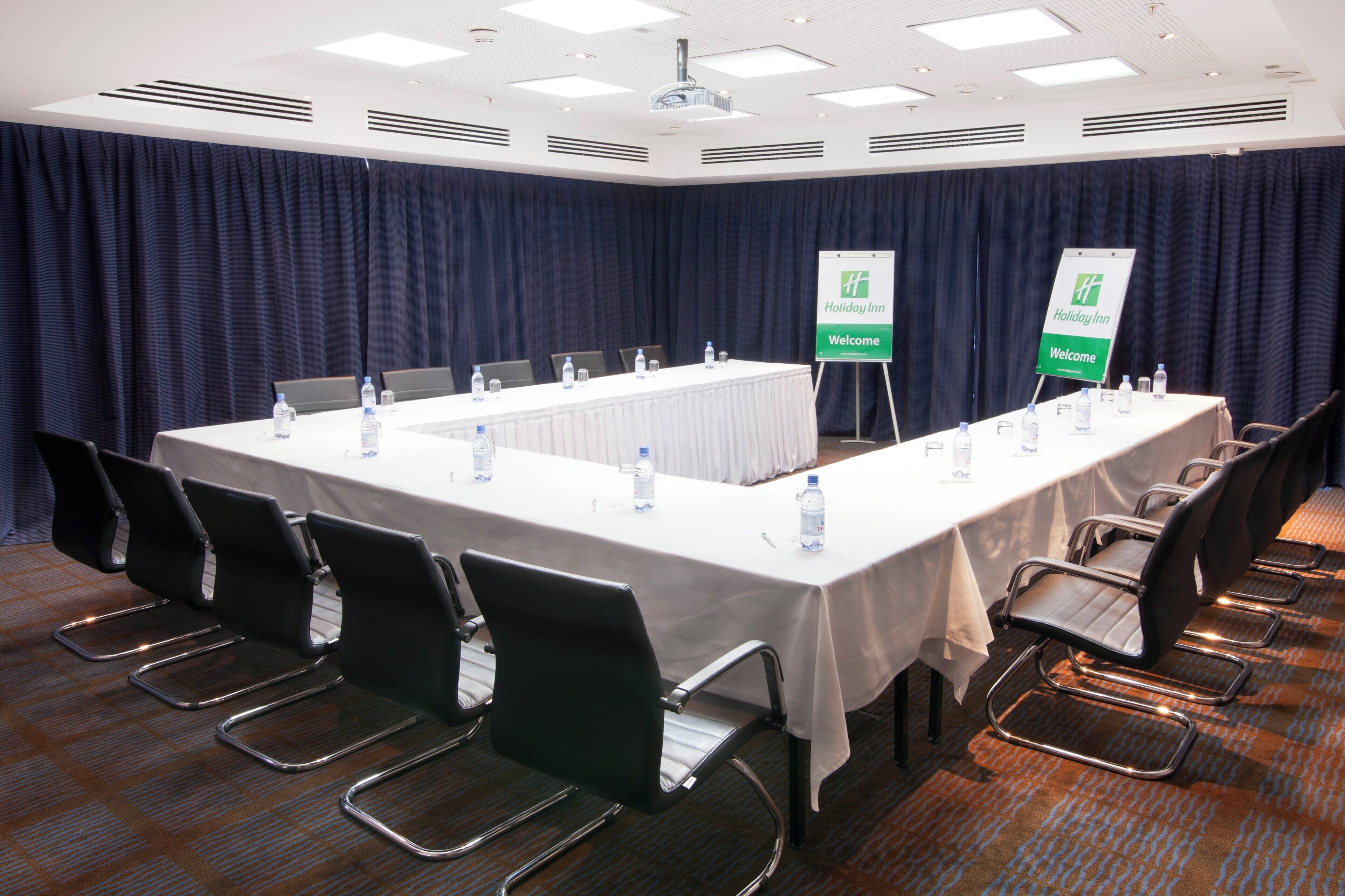 A conference room with a long table, chairs, and two Holiday Inn welcome signs.
