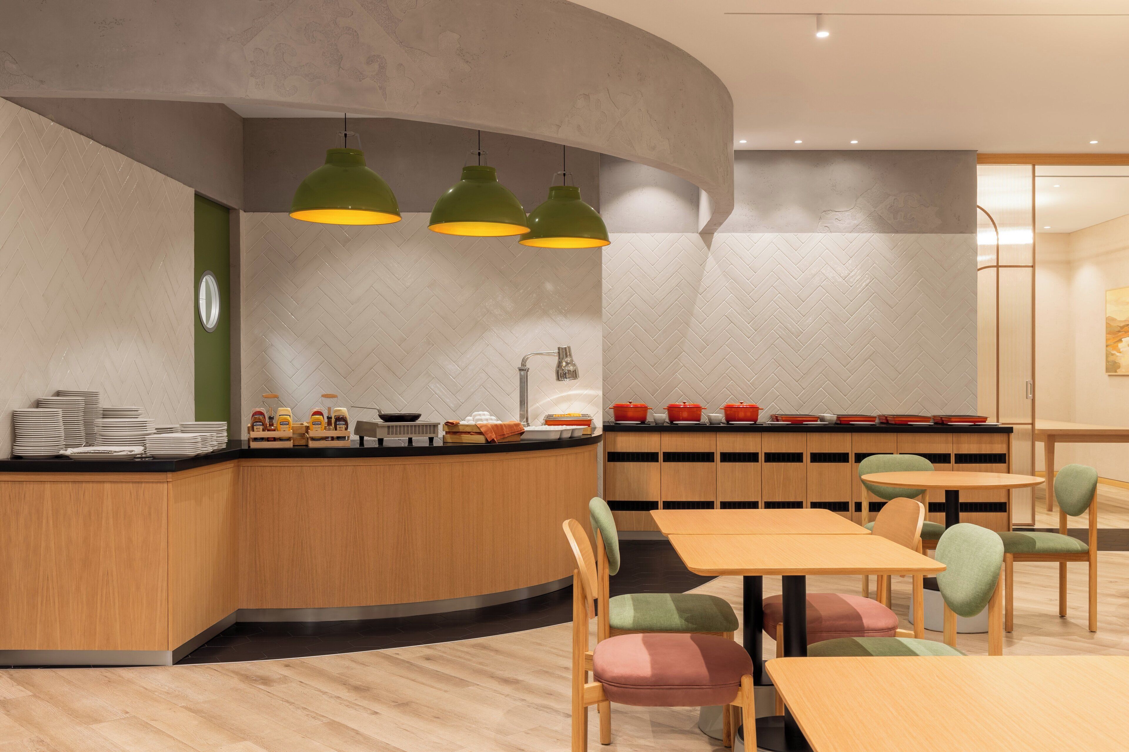 Een modern restaurant met een gebogen balie, groene hanglampen en diverse zitmogelijkheden, waaronder tafels en stoelen.