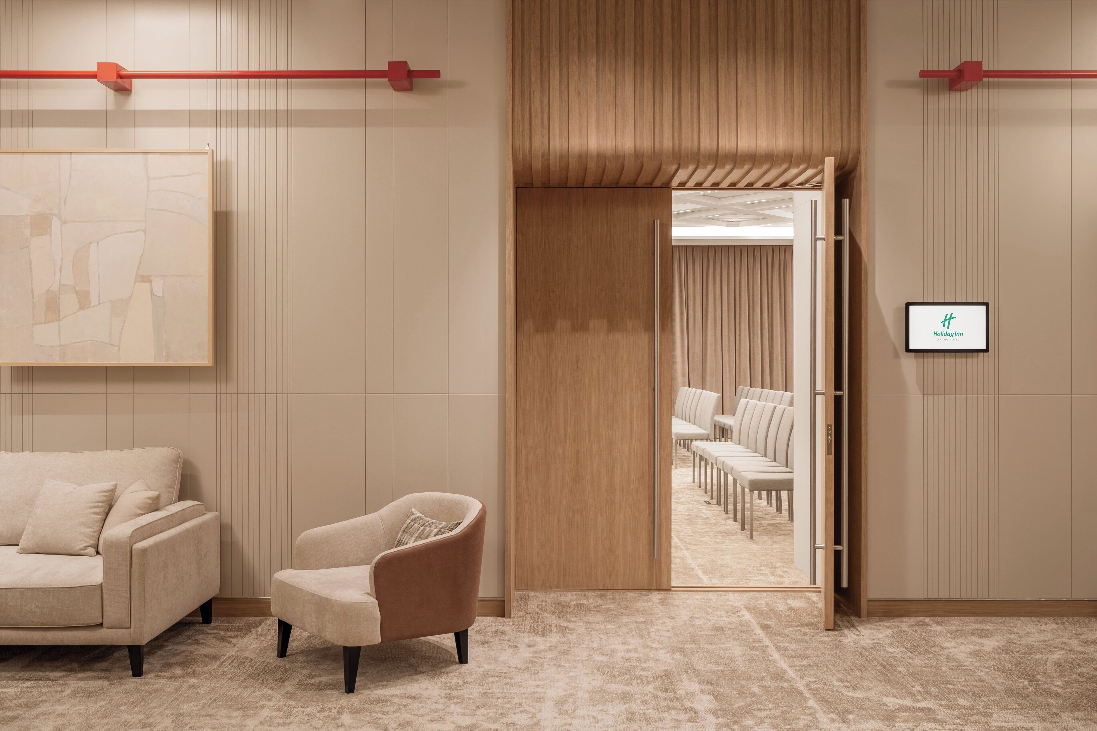 A hotel lobby with a beige sofa, armchair, and a wooden partition leading to a seating area.