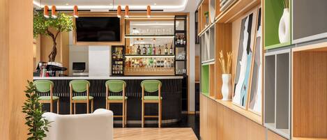 A modern bar area with a wooden bar counter, green chairs, and a television mounted above.