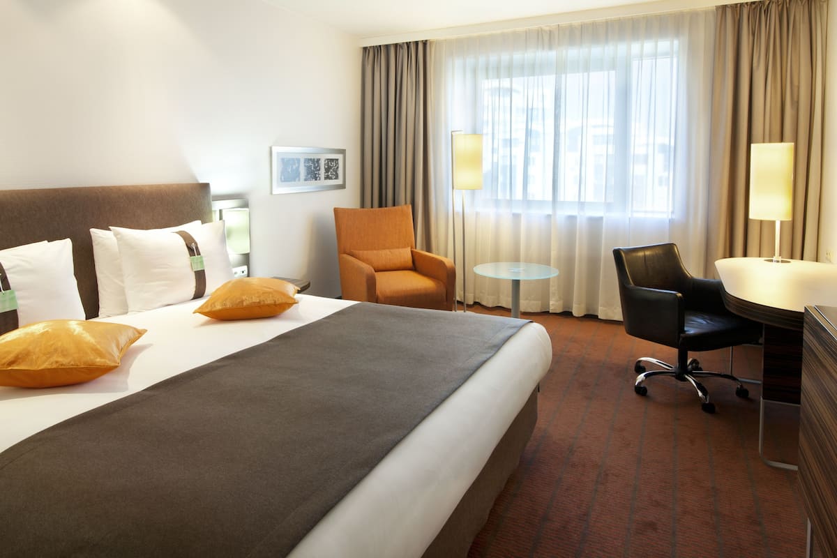A hotel room with a large bed, two armchairs, a desk, and a small table.