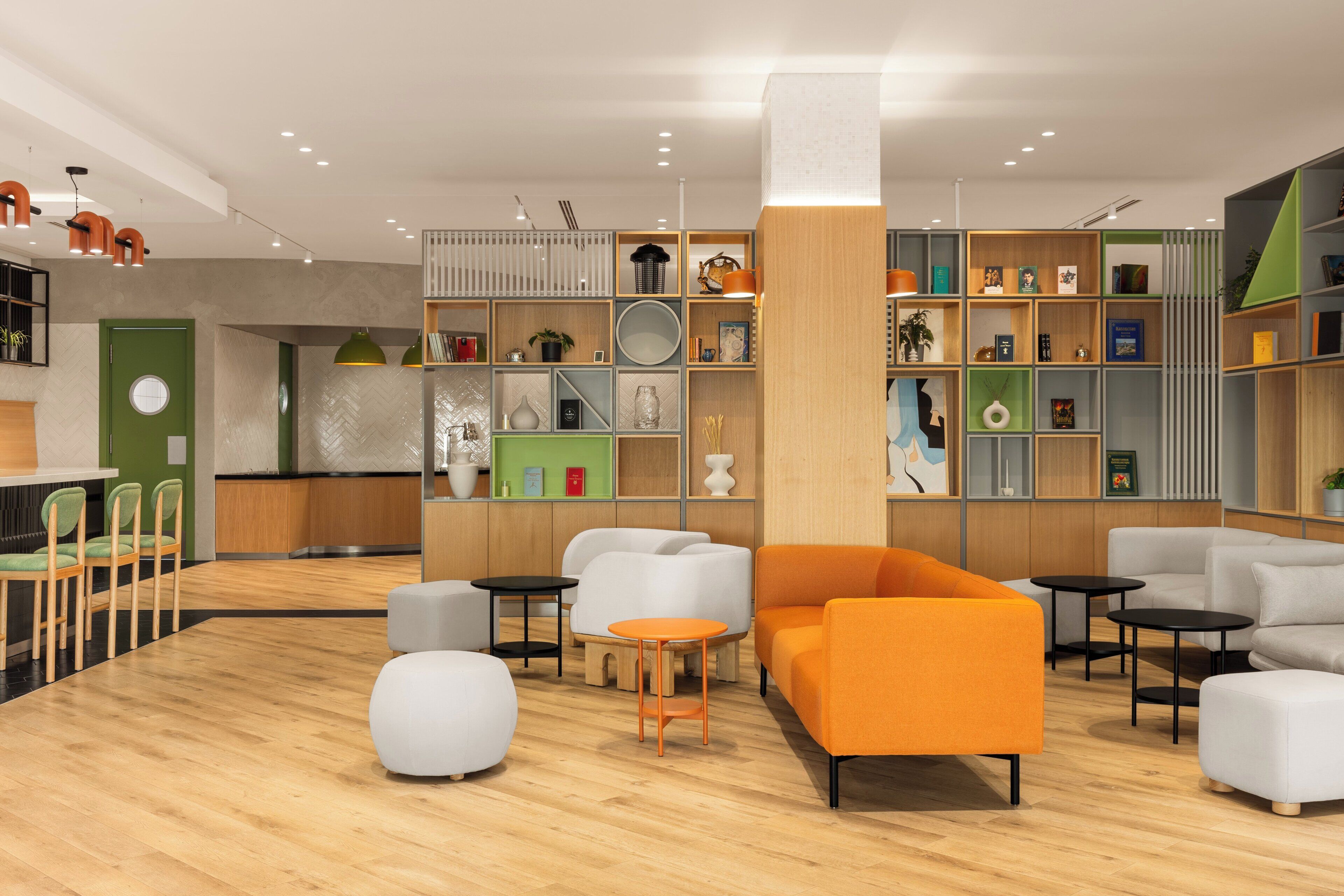 A modern interior with a wooden floor, a green door, and a seating area with an orange sofa and white chairs.