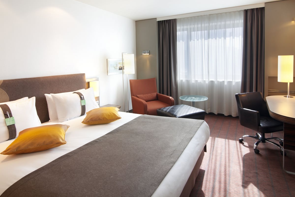 A hotel room with a large bed, a desk, a chair, and a small table.