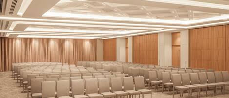 Un salón de conferencias con hileras de sillas, piso alfombrado y un diseño moderno en el techo.