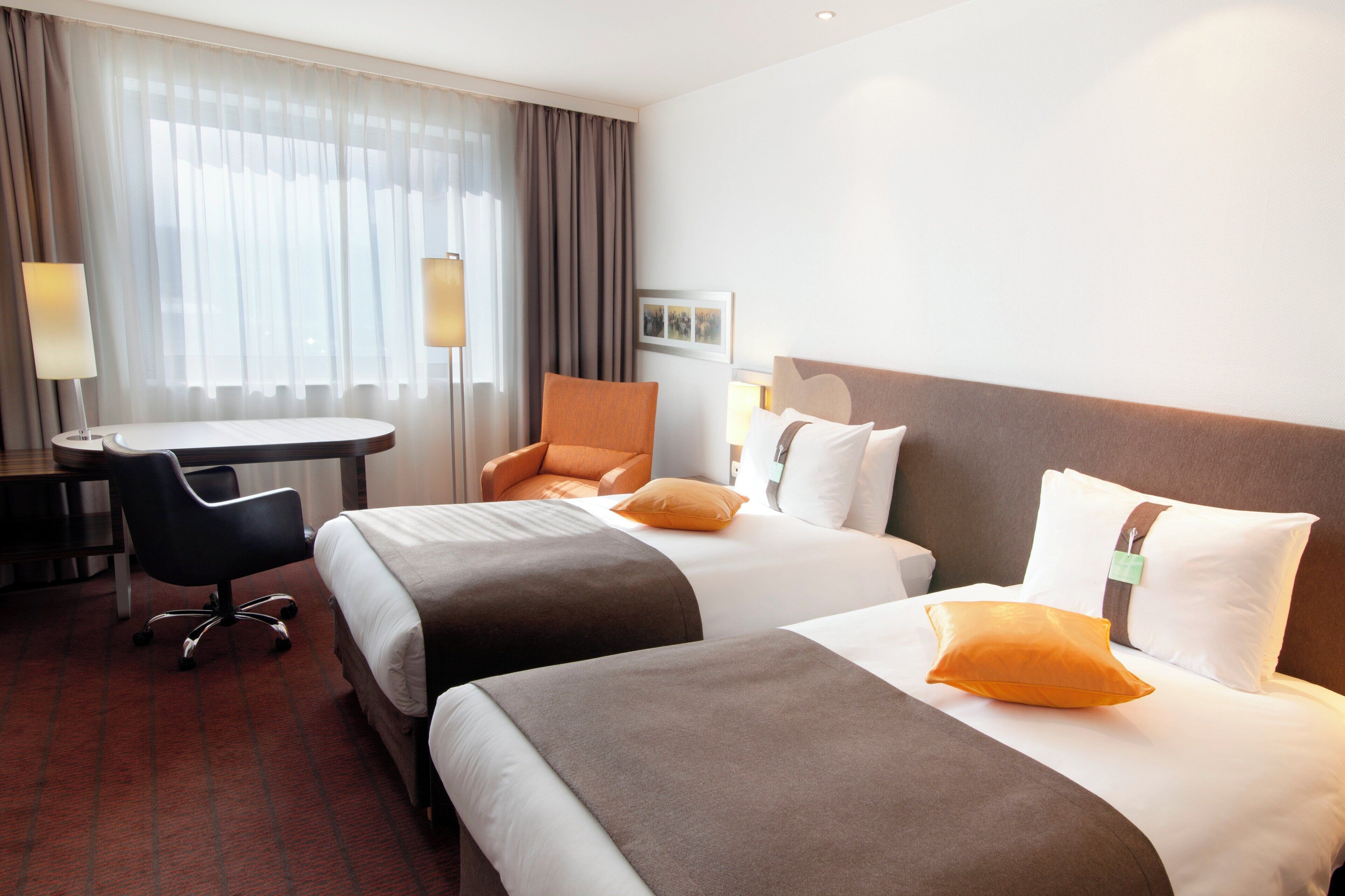 Habitación de hotel con dos camas, un escritorio, una silla y una lámpara.