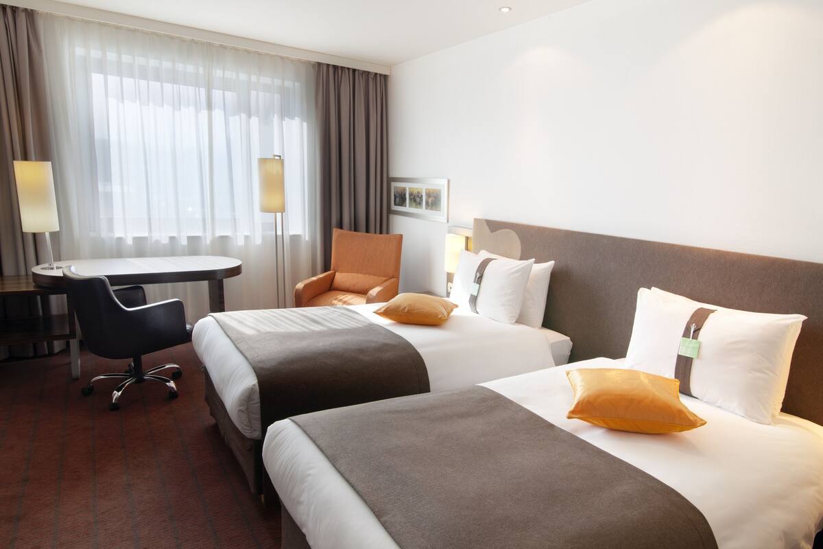 A hotel room with two beds, a desk, and a chair.