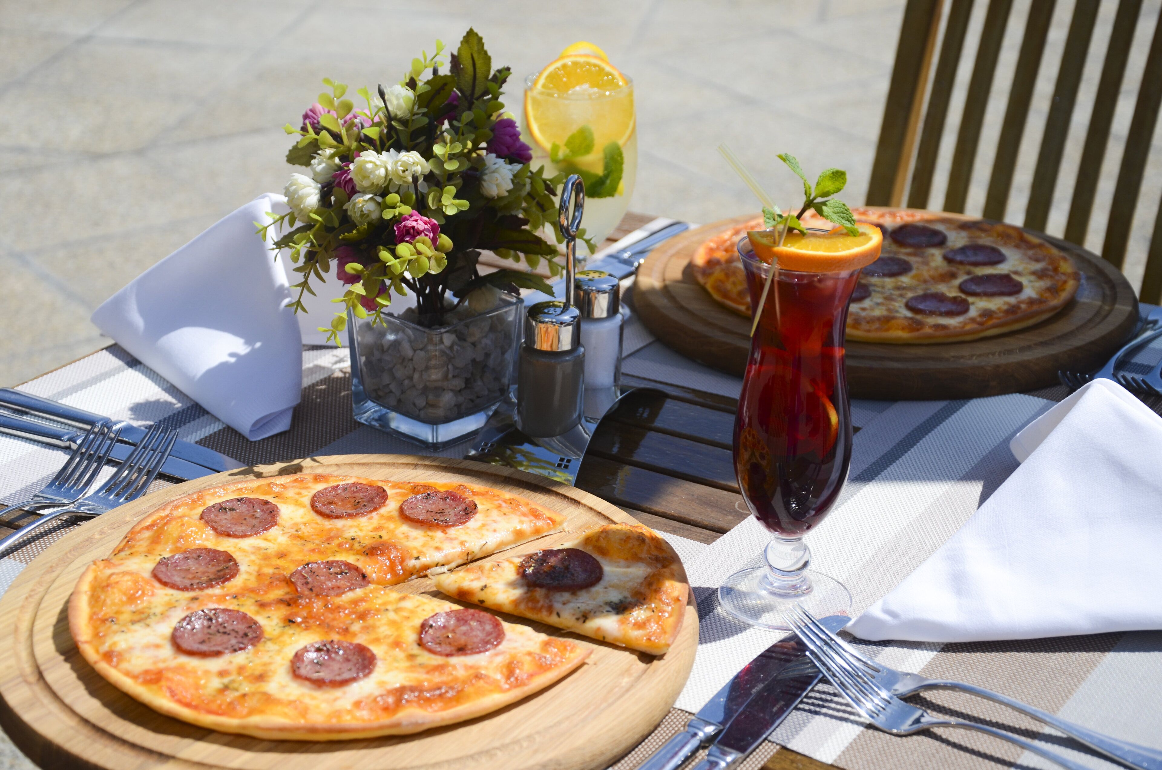 Una mesa con una pizza, una bebida y un arreglo floral.