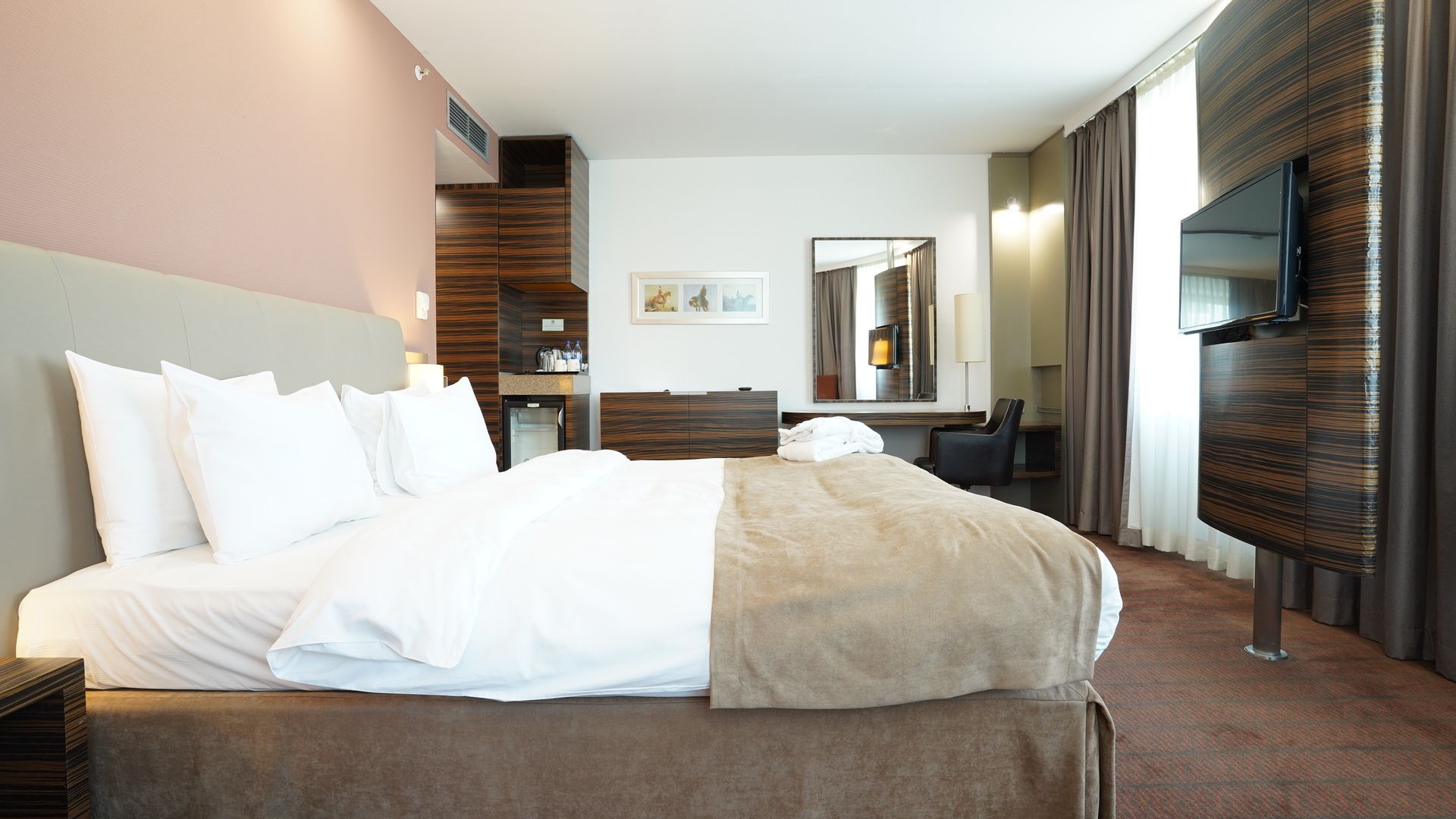 Une chambre d’hôtel avec un grand lit, un bureau, une chaise, une télévision et un miroir.