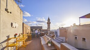 Une terrasse sur le toit, avec des chaises et des tables jaunes, un banc en bois et une vue sur une tour en arrière-plan.