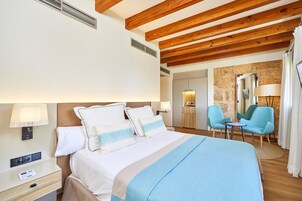 Una habitación de hotel con cama, mesitas de noche, escritorio, sillas y una pared de piedra.