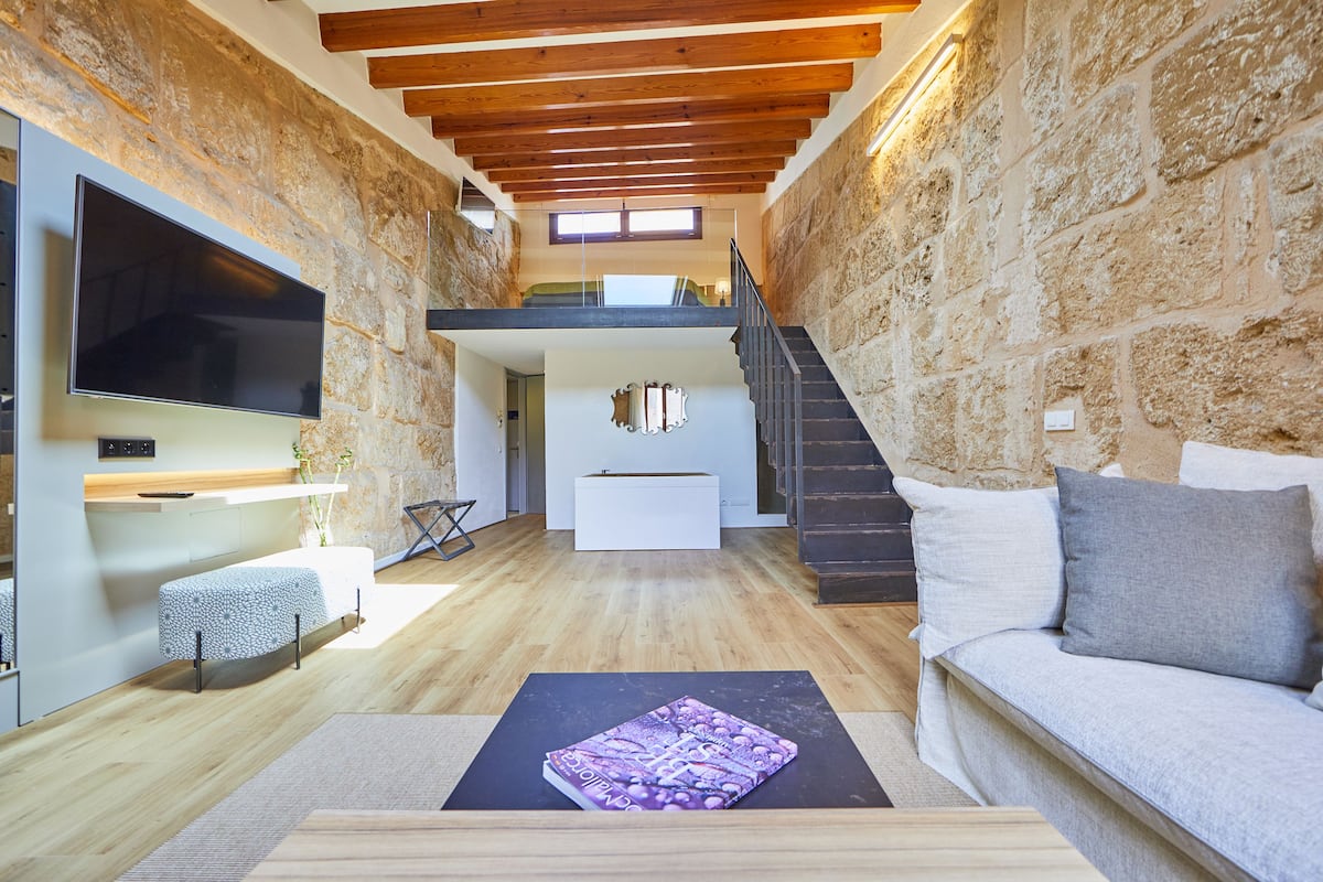 Ein modernes Wohnzimmer mit Steinwänden, Holzboden und einer flachen Decke, einem Flachbildfernseher, einer Couch und einem Couchtisch mit einem Buch.