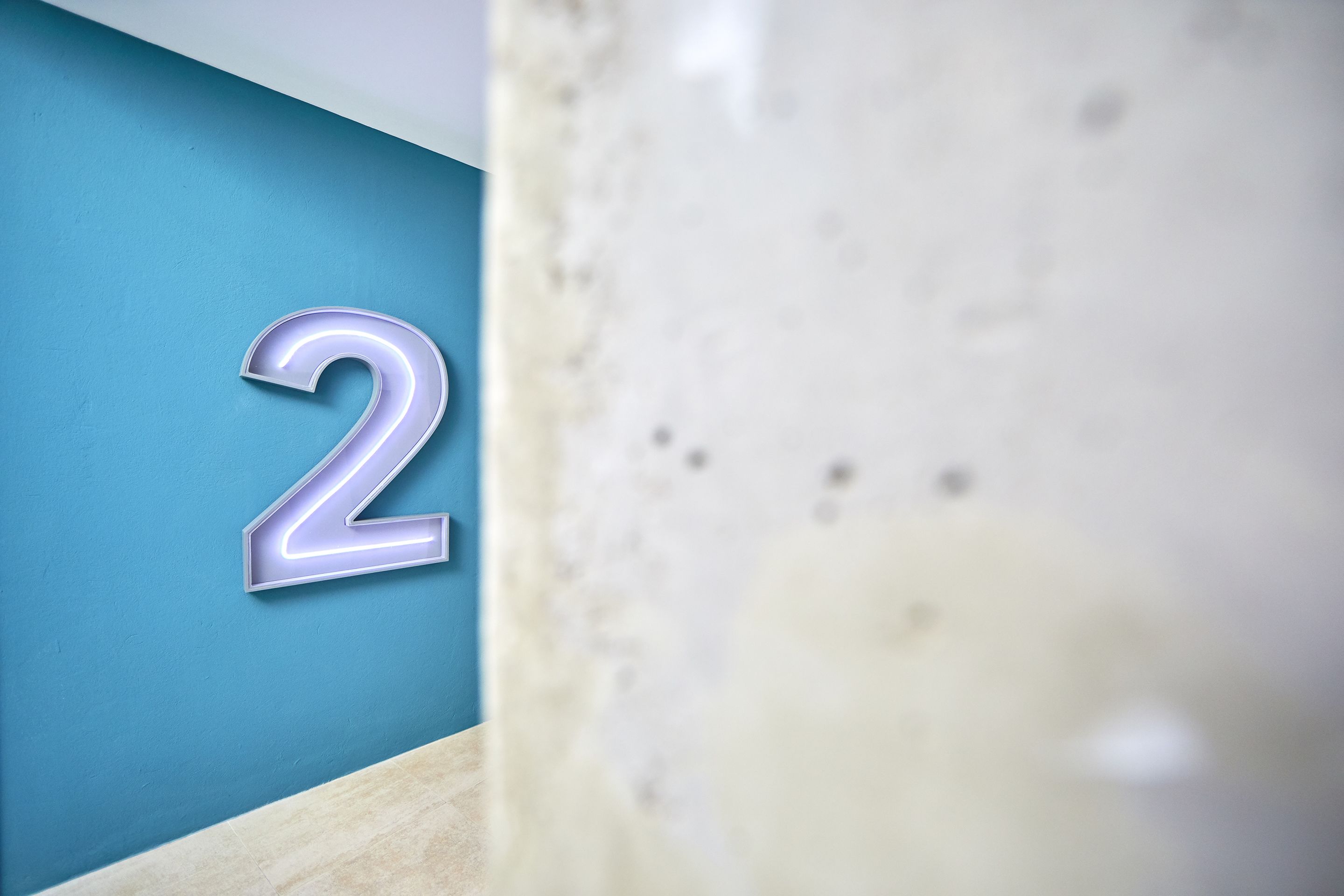 Primer plano de una pared con el número '2' grande e iluminado y una porción de superficie con textura.