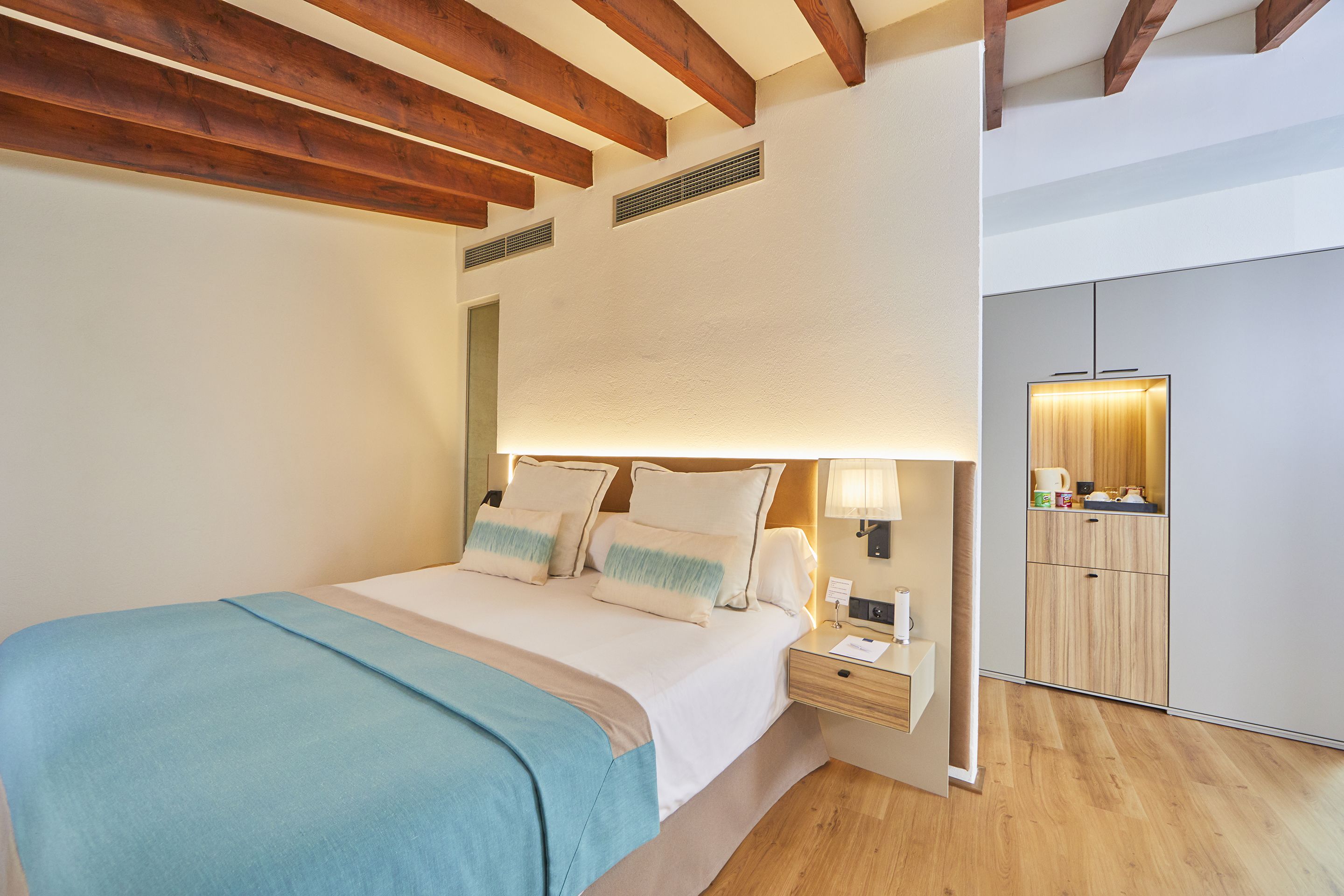 A bedroom with a bed, bedside table, lamp, and a view of a bathroom.