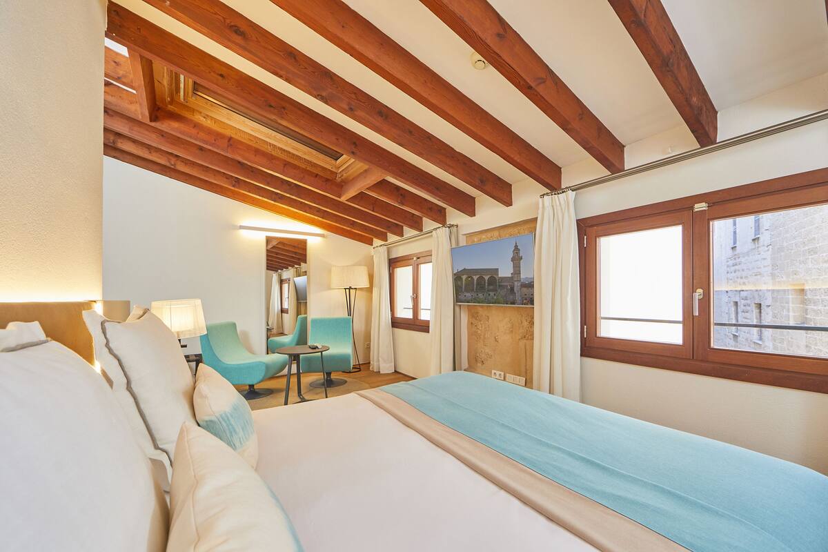 Ein Hotelzimmer mit Bett, Schreibtisch, zwei Stühlen und einem Fenster mit Blick auf ein Gebäude.