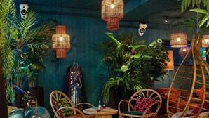 Een kamer met rieten stoelen, een oldtimer en hangende rieten lampen.