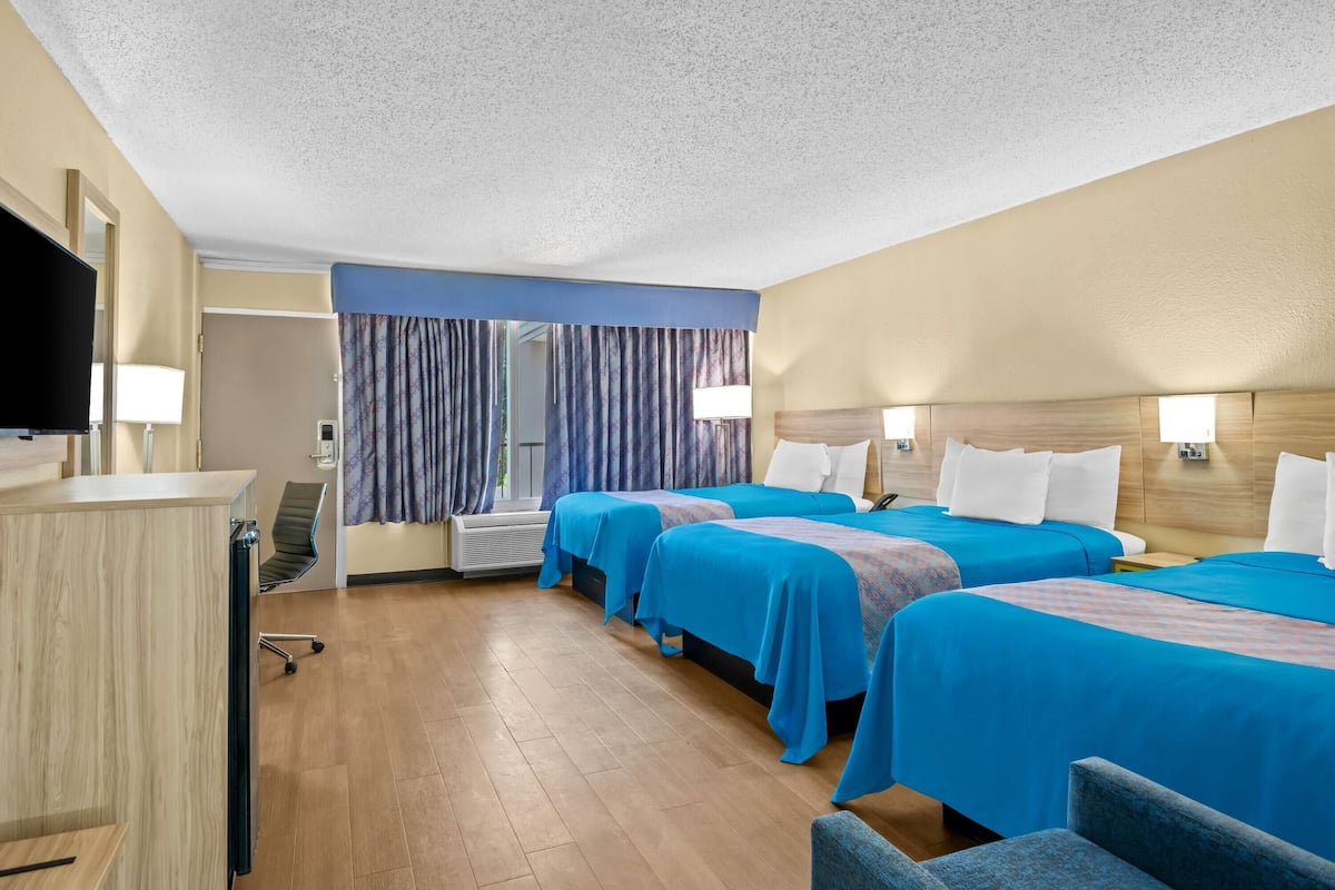 Une chambre d’hôtel avec deux lits, un bureau, une télévision et une fenêtre avec des rideaux.