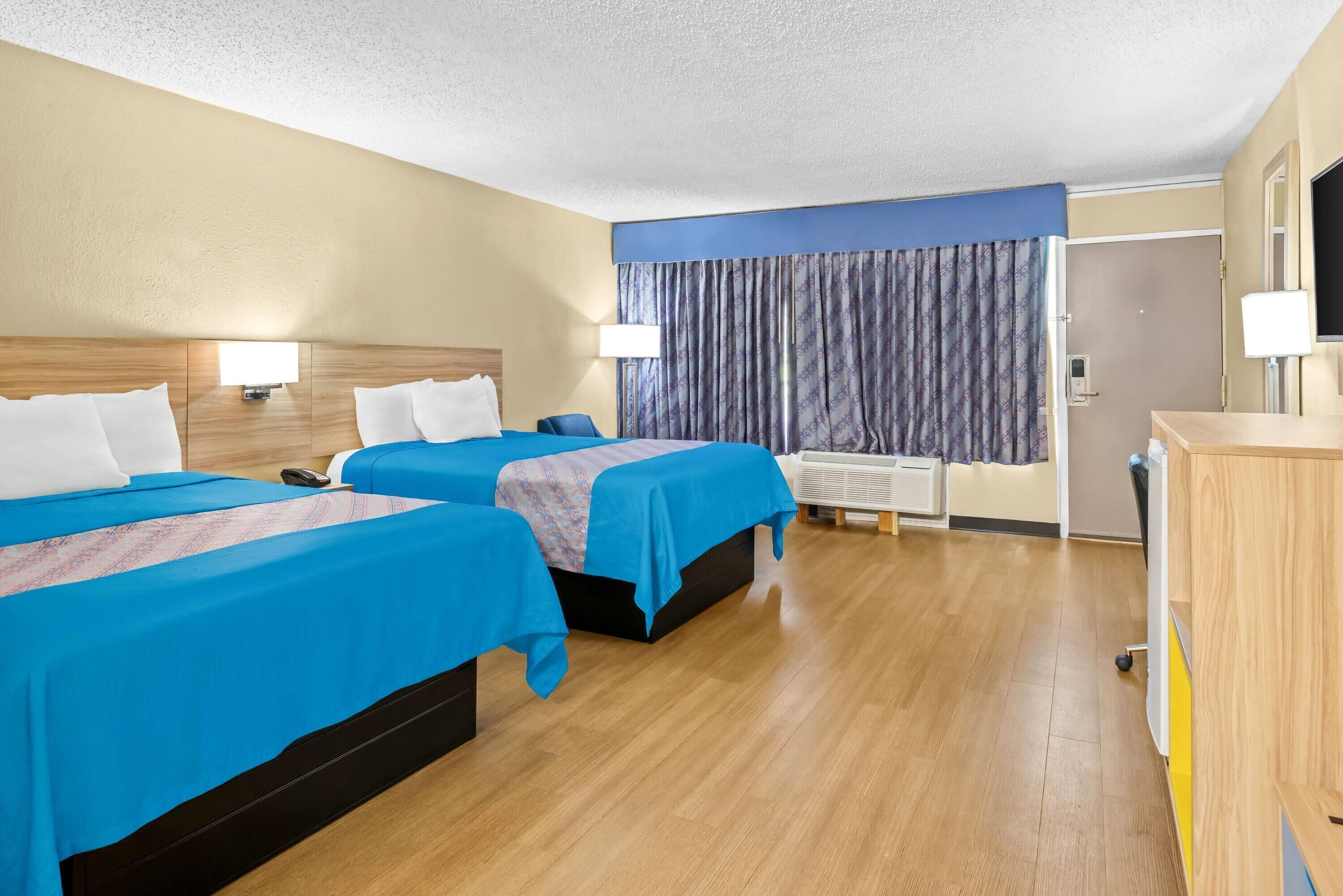 Une chambre d’hôtel avec deux lits, des têtes de lit en bois et un bureau avec une chaise.