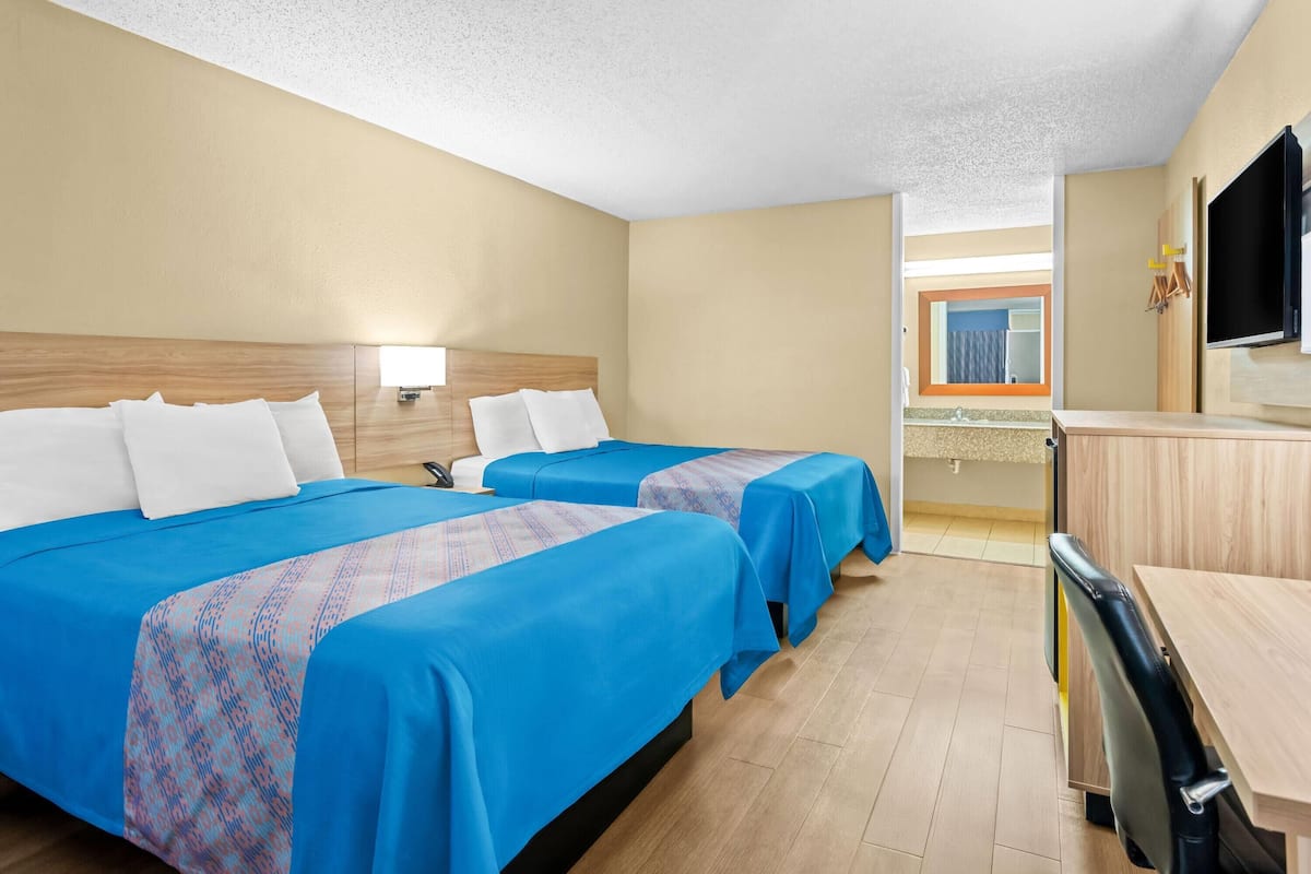 Une chambre d’hôtel avec deux lits, un bureau, une télévision et une salle de bain visible à travers une porte ouverte.