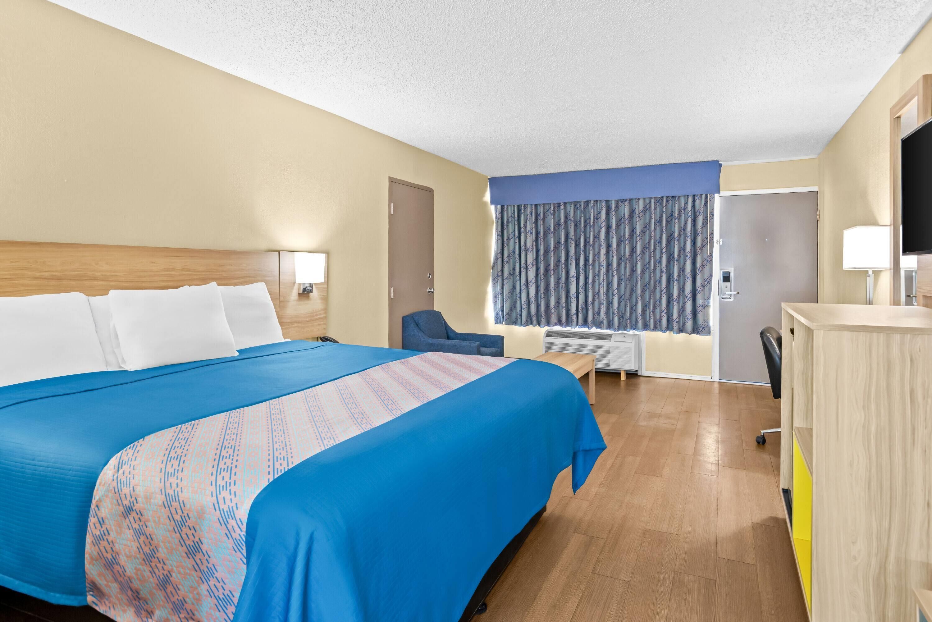 A hotel room with a large bed, a desk, a chair, a TV, and a window with curtains.