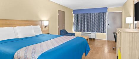 A hotel room with a large bed, a desk, a chair, a TV, and a window with curtains.