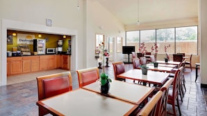 Un amplio comedor con mesas y sillas de madera, un quiosco Daybreak y grandes ventanales que ofrecen vistas al exterior.
